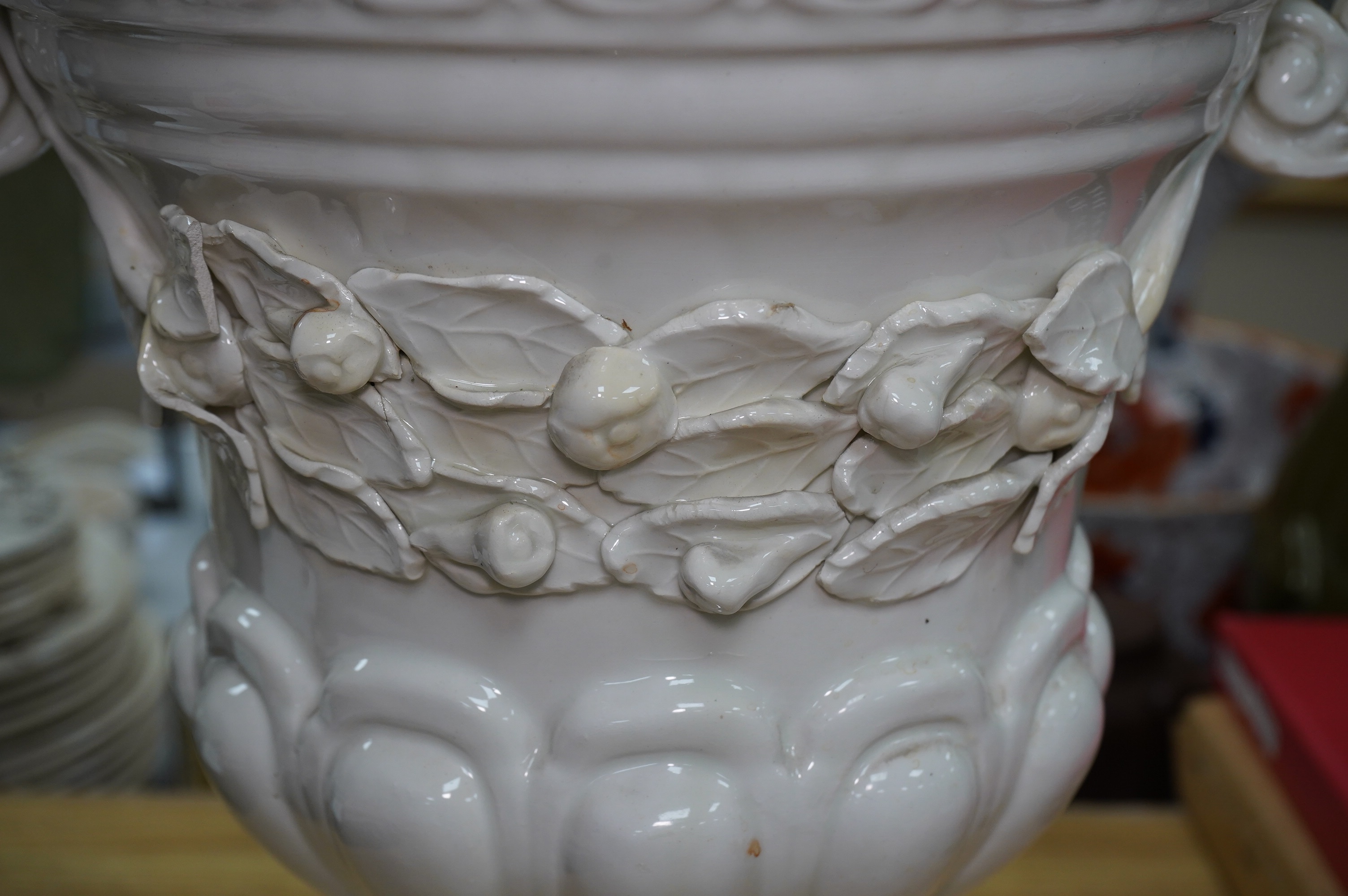 A large cream glazed pottery pedestal vase, with decorative swag of fruit and leaves, 43cm high. Condition - corner of square base broken, glazing chipped on top rim and fruit and leaf decoration broken